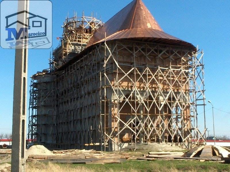 Biserică în execuție, înconjurată de schele, cu învelitoare de cupru montată