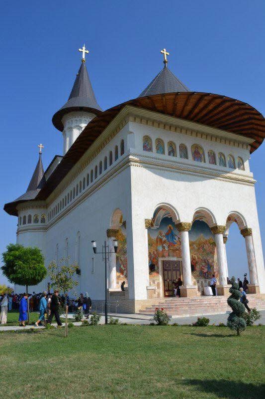 Biserică finalizată, fațadă albă, turle și pridvor cu picturi